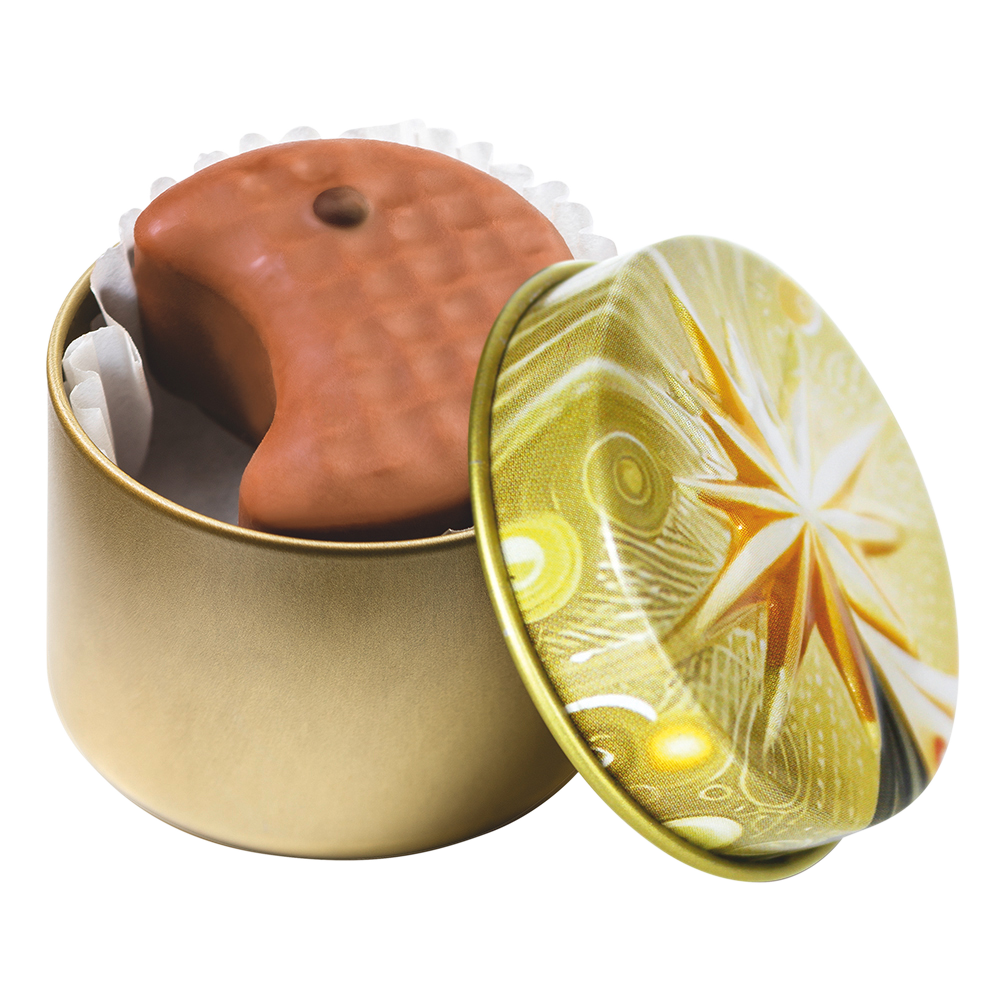 Geöffnete kleine goldene Metalldose mit Weihnachtsstern-Motiv und einer halbmondförmigen Vollmilch-Praline 