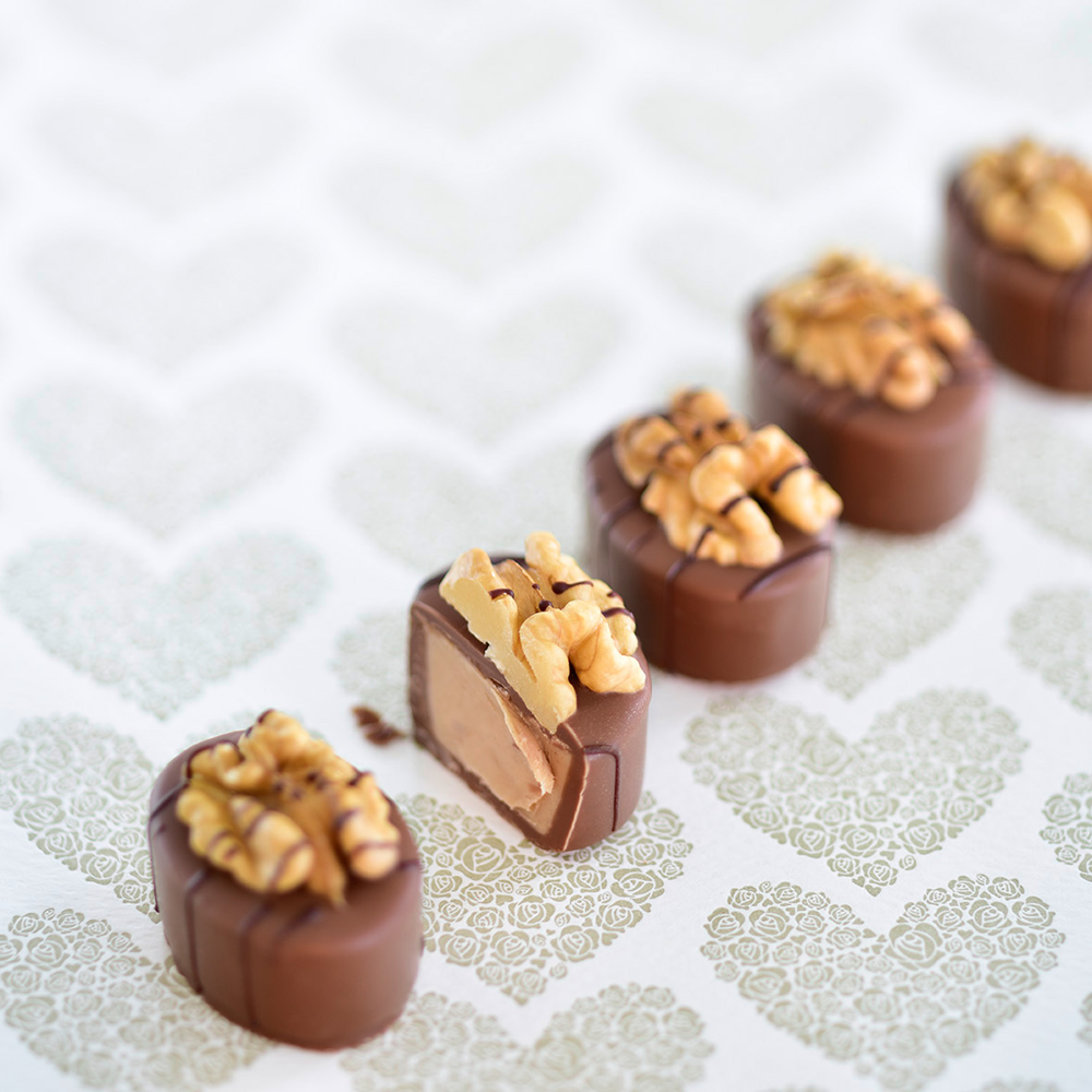 Fünf Walnuss-Nougat-Pralinen aus Vollmilchschokolade mit Walnusshälften dekoriert; eine Praline ist angeschnitten und zeigt die cremige Nougatfüllung