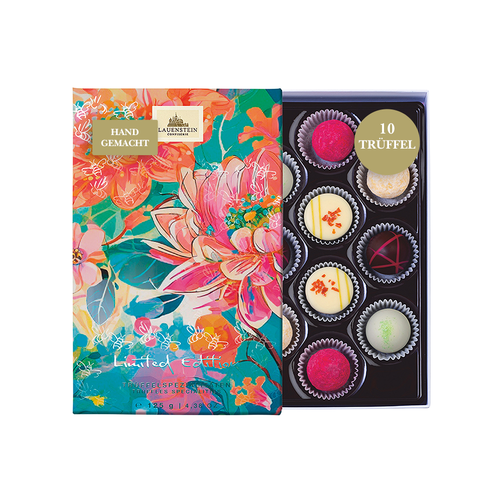 Geöffnete Lauensteiner Pralinenpackung im floralen Aquarell-Design mit gold-geprägten Bienen neben zehn handgemachten Pralinen und Trüffeln
