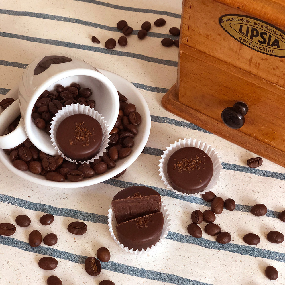 Runde Espresso-Pralinen umhüllt von dunkler Schokolade dekorativ angerichtet neben einer Kaffeemühle und Kaffeebohnen