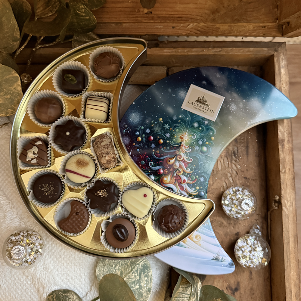 geöffnete Pralinen-Dose in einer Holzkiste neben glitzernden Christbaumkugeln