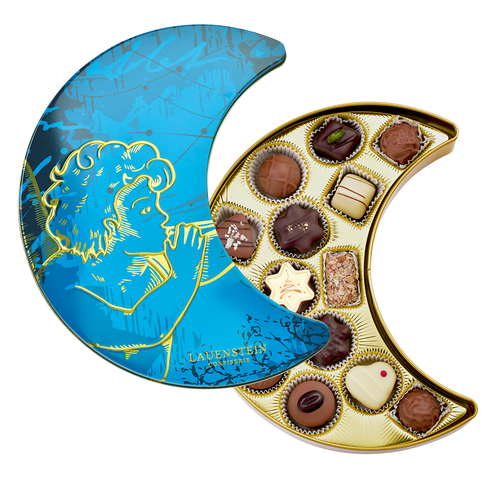 blaue Lauensteiner Geschenkdose aus Metall in Mond-Form mit Engel-Motiv, halb geöffnet und befüllt mit verschiedenen feinen Pralinen und Trüffeln