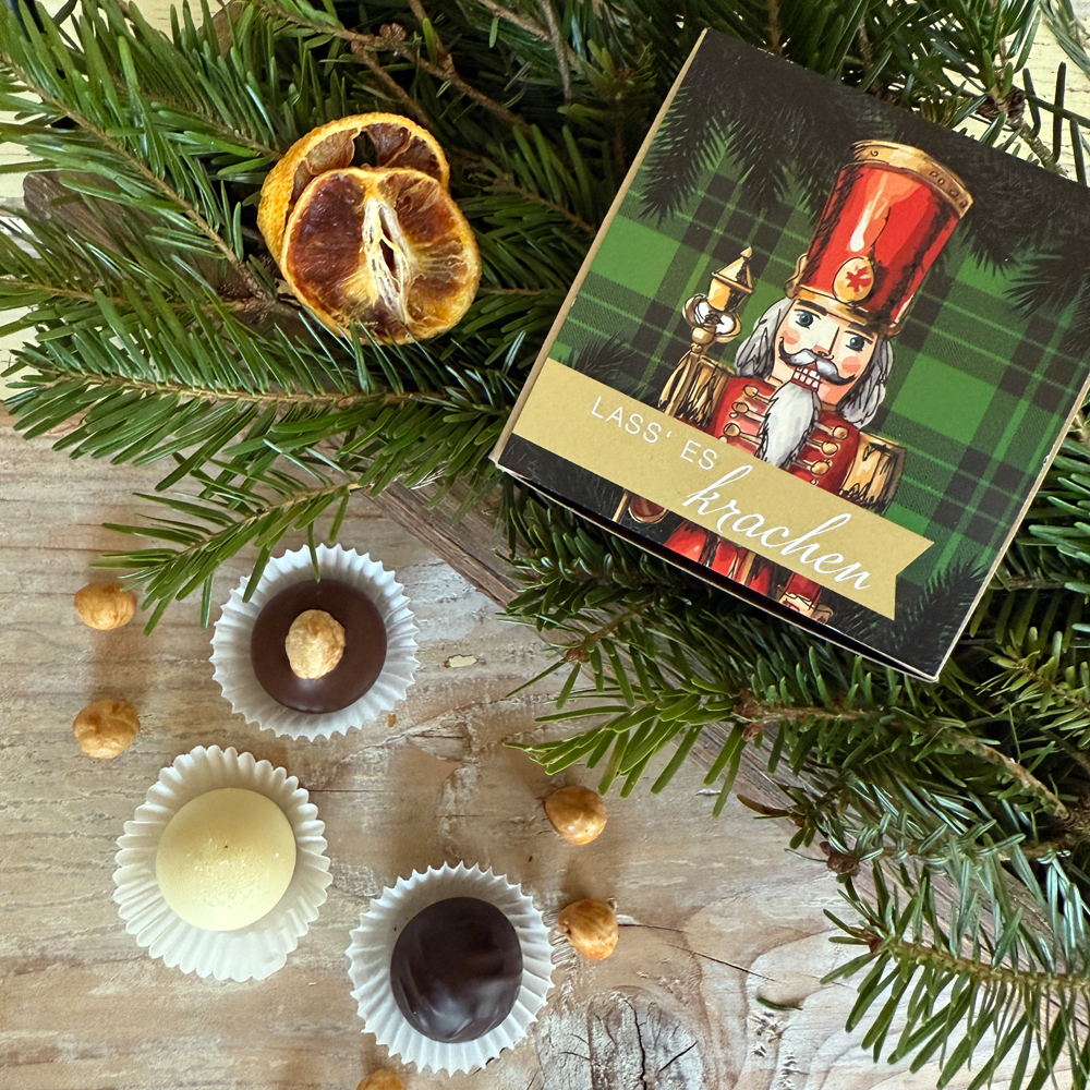 Weihnachtliches Lifestyle-Motiv mit Pralinenschachtel, drei einzelnen Pralinen und Tannengrün