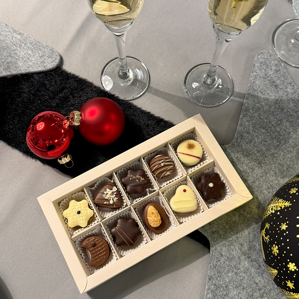 geöffnete Pralinenschachtel auf festlichem Tisch mit Christbaumkugeln und Sektgläsern