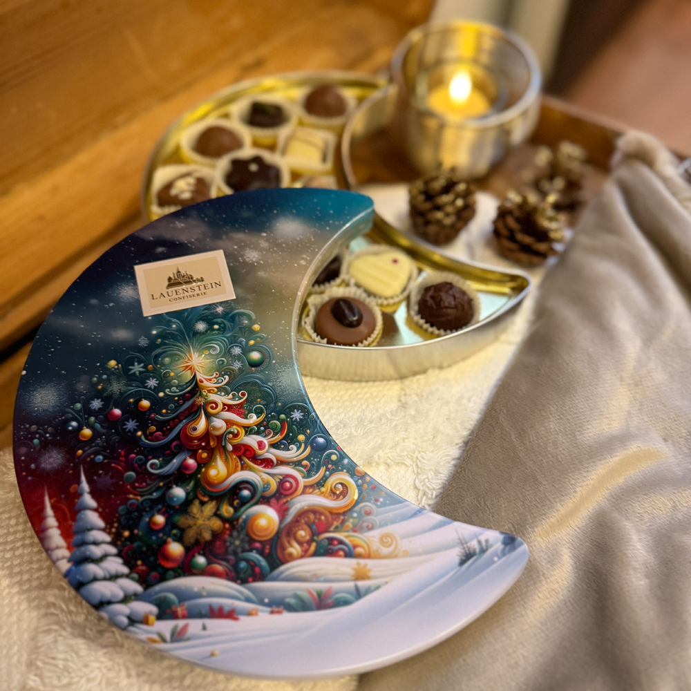 halb geöffnete Pralinendose in weihnachtlicher Kulisse mit Tannenzapfen, Teelicht und einer kuscheligen Decke