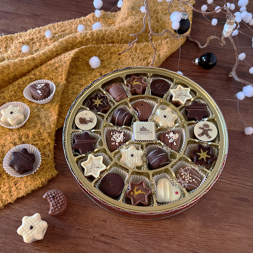 Runddose eingebettet in weihnachtliche Dekoration mit einer bunten Auswahl an Pralinen 