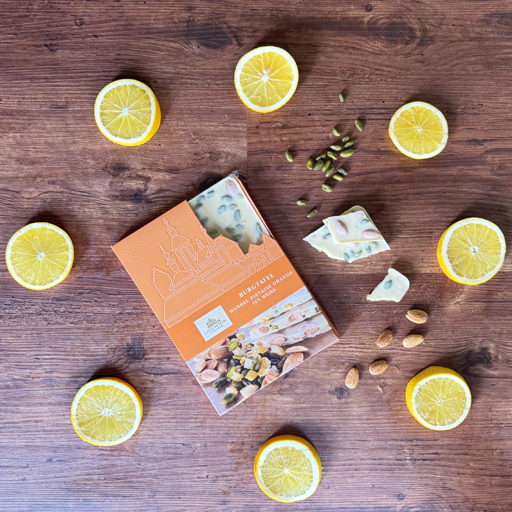 Orange Lauenstein Schokoladenverpackung umgeben von frischen Orangenscheiben, Schokostücken, Mandeln und Pistazien