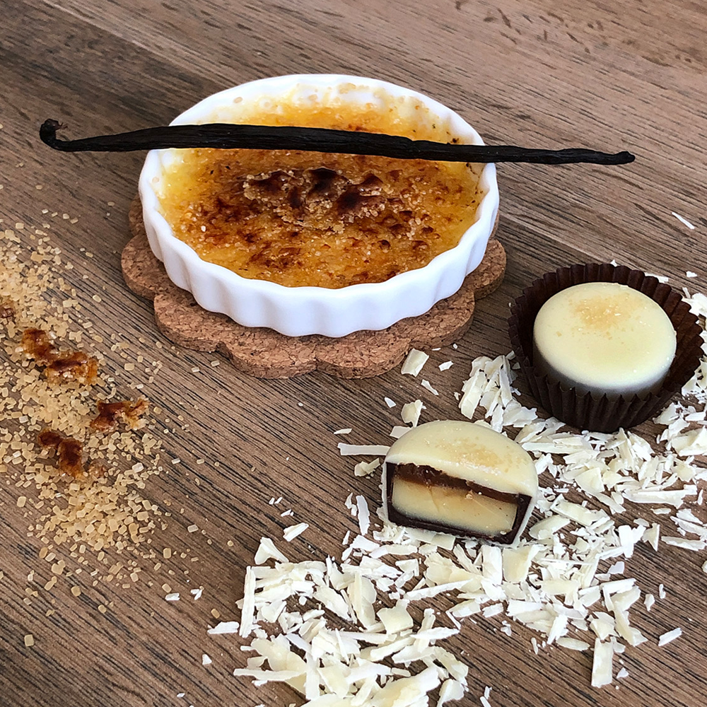 Crème-Brûlée-Trüffel mit Anschnitt, dekorativ angerichtet mit karamellisierter Crème brûlée, Vanilleschote und Schokoladenspänen