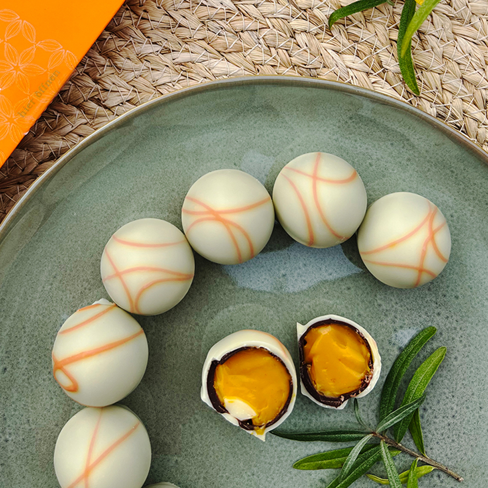 Weiße Pralinen mit feiner orangefarbener Verzierung und fruchtiger, orangefarbener Füllung auf grünem Teller