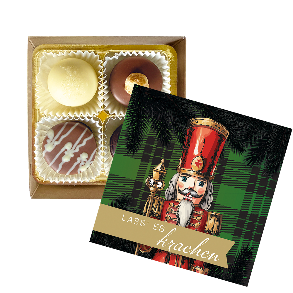 Geöffnete Pralinenschachtel mit vier unterschiedlichen Pralinen ohne Alkohol neben Deckel mit Nussknacker-Motiv und Aufschrift Lass es krachen