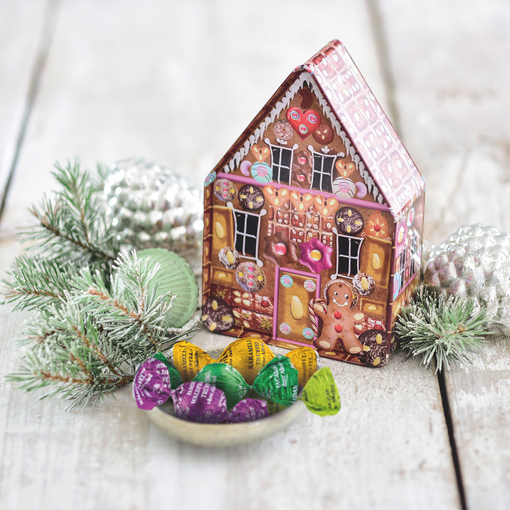 Dose auf hellem Holzgrund, dekoriert mit einzeln verpackten Gourmetkugeln, Christbaumkugeln und Tannenzweigen