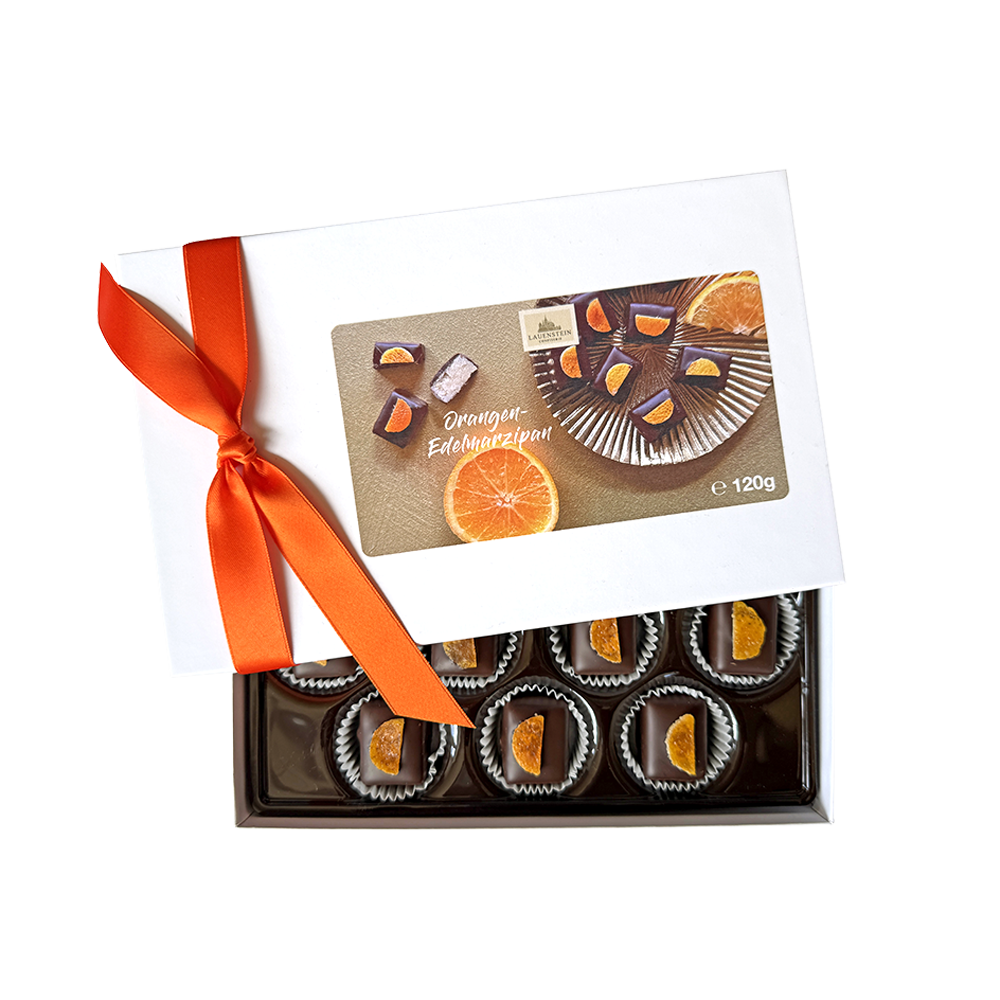 Dunkle Orangen-Edelmarzipan-Pralinen von Lauenstein in halb geöffneter, weißer Geschenkbox mit orangefarbener Schleife