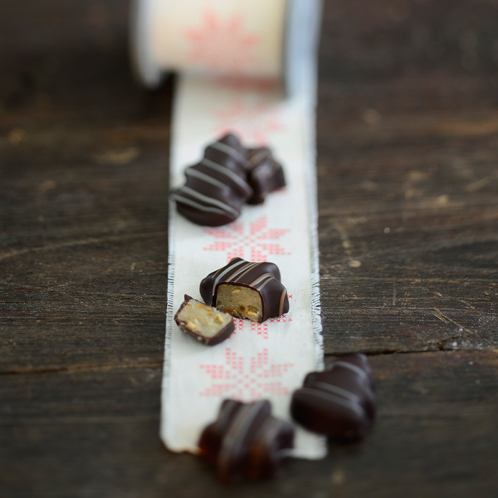 Dunkle Pralinen in Stern- und Tannenbaumform mit Marzipan-Füllung auf einem weihnachtlich dekoriertem Tisch