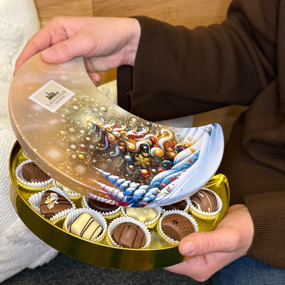Zwei Hände öffnen den Deckel der Mond-Dose, um die feinen Trüffelpralinen zu präsentieren