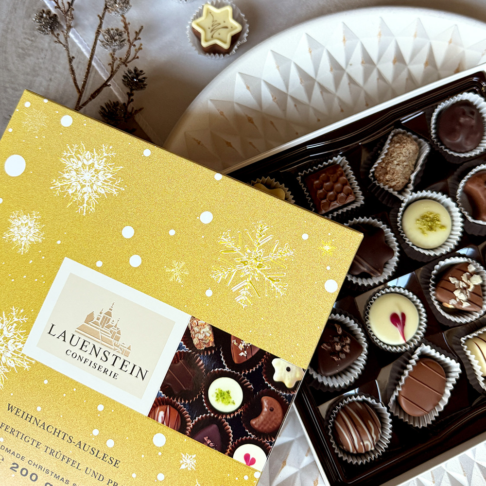 Schräg geöffnete Pralinenschachtel mit feinen Trüffeln auf einem weißen Dekoteller