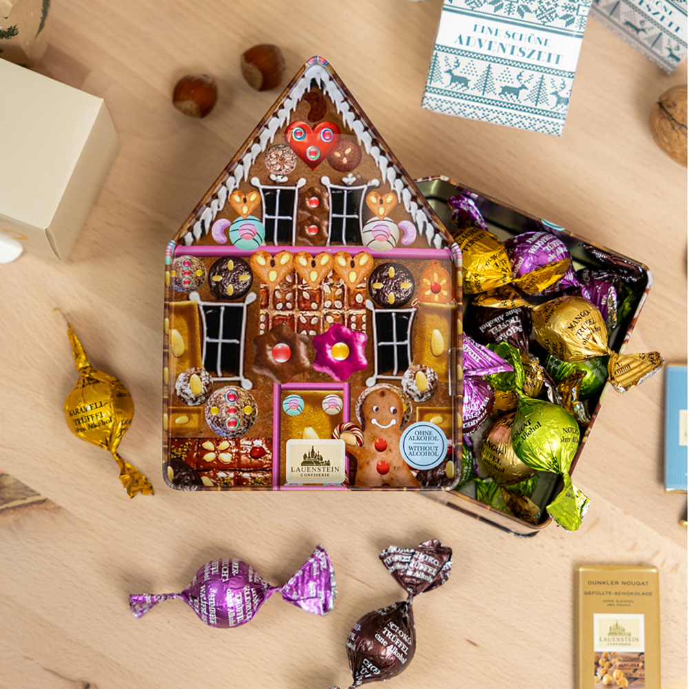 geöffnete Dose mit verschiedenen Gourmetkugeln, umgeben von Nüssen und Adventsdeko