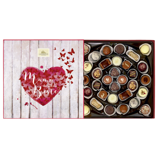 Geöffnete Pralinenschachtel mit Muttertagsmotiv: Auf dem Deckel ein rotes Herz mit Schmetterlingen und der Aufschrift Mama, du bist die Beste. Daneben eine große Auswahl verschieden dekorierter Pralinen und Trüffel in einer runden Anordnung.