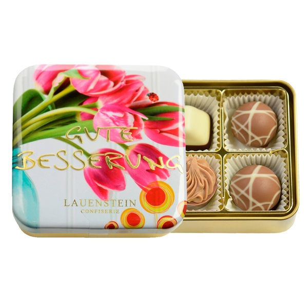 Geöffnete goldene Lauenstein Metalldose Gute Besserung mit Tulpen-Motiv neben vier Pralinen