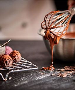 Schneebesen mit leckerer Vollmilchschokolade neben fertigen Pralinen